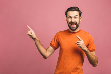 Wall Mural - Look over there! Happy young handsome man in casual pointing away and smiling while standing against pink background.