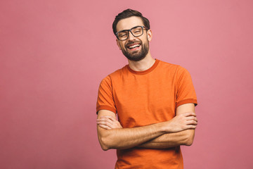 Happy young man. Portrait of handsome young man in casual keeping arms crossed and smiling while standing against pink background.