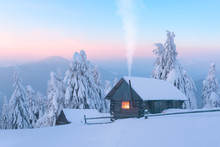 Fantastic Winter Landscape With Wooden House In Snowy Mountains. Smoke Comes From The Chimney Of Snow Covered Hut. Christmas Holiday And Winter Vacations Concept