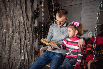 Wall Mural - father and daughter reading a book sitting on a swing