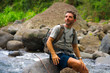 © TheVisualsYouNeed - young happy and attractive man with travel backpack hiking in river at forest feeling free enjoying nature and fresh environment on summer trekking journey
