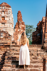 Portrait of stylish woman in white dress admiring landscape while posing near ancient ruins somewhere in Asia. Summer vacation, adventures concept. Vertical shot. Rear view.