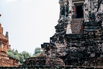 Portrait of attractive tourist girl on vacation posing in ancient ruins of old temple while having photoshoot in white dress. Summer trip, tourism, adventures concept. Horizontal shot