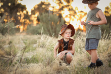 Young Boys Dressed Up As Cowboys In An Open Field With Long Grass And A Vibrant Sunset In The Background