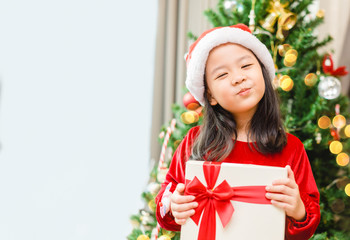 Little asian girl smile and excited and holding red gift box on christmas tree and white background.Child girl holding gift box in Christmas celebration and Happy New year concept.