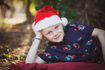 Child dressed in Christmas outfit  on  red blanket in the park with a decorated Christmas tree in the background