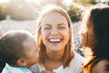 Wall Mural - portrait of a beautiful young mother laughing while closed eyes while her little daughter and son ar