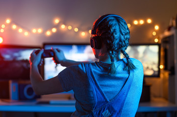 Wall Mural - Gamer or streamer girl at home in a dark room with a gamepad playing video games with friends online. Young man sits in front of a monitor