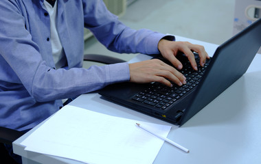 unknown man is typing on laptop and taking notes on empty white paper 