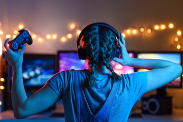 Wall Mural - Games online, a young girl playing computer games using a joystick or a gamepad. On three large monitors, creative light. Strategies, racing and gaming business