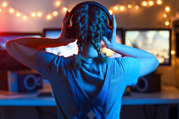 The girl emotionally plays video games with a headset on the computer online with her friends.