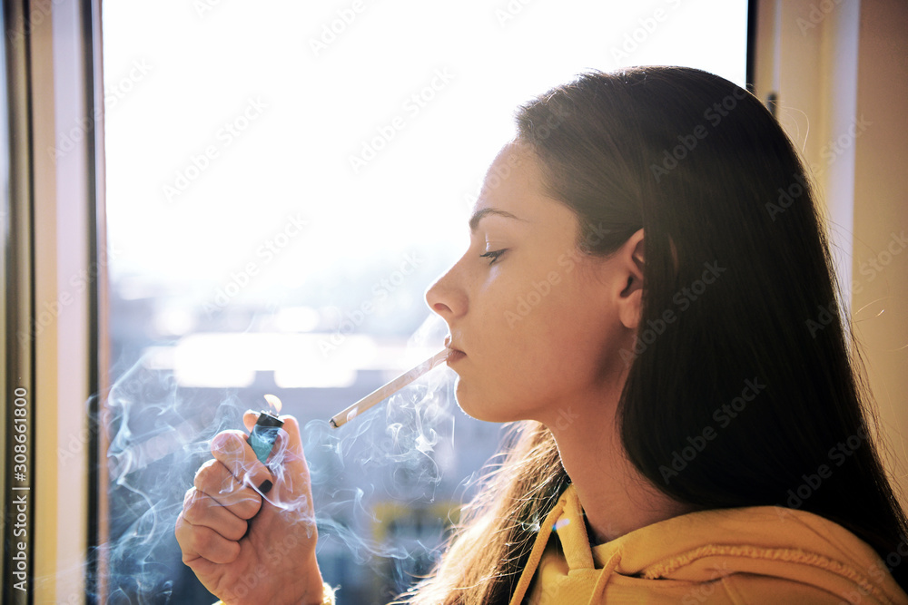 Beautiful attractive girl smoking a cigarette at the window. Pretty woman  smoking cigarette. Stock Photo