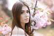 © ElenaBatkova - Portrait of a beautiful young woman model near pink branches with Sakura flowers.