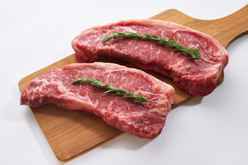 Wall Mural - Striploin steaks being prepared for cooking. Two fresh raw beef steak on wooden board on white background with rosmary.