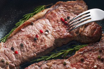 Wall Mural - Concept for a tasty and healthy meal. Close-up shot of gourmet grilled steak in a iron pan for dinner. Seasoned with spices and a sprig of rosemary.