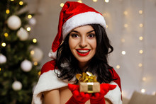 Beautiful Sexy Girl Wearing Santa Claus Clothes With Christmas Gift Box On The Background Of The Christmas Tree