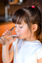 Adorable smiling little girl drinking water in kitchen. Health and beauty concept