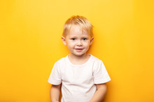 2 Years Portrait Of Little Blond Happy Caucasian Blue Eyes Baby Boy Wearing On White T Shirt On Yellow Background With Copy Space