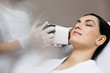 © 58production - Hardware cosmetology. Skin surface scanning technology. Portrait of a beautiful woman in a cosmetology clinic with professional female cosmetologist doing a procedure on the skin.