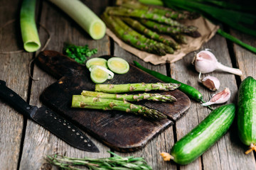 Green raw asparagus and green fresh vegetables on a wooden table