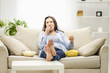 © Andrii - Portrait of pretty, charming, cheerful woman with straight black hair, who is eating pop corn and potato chips, watching comic serial, comedy, sitting with crossed legs in living room.