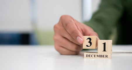 close up employee man hand put number _ of cube shape wood to make calendar date December 31 at office desk for the last day of the last year countdown concept