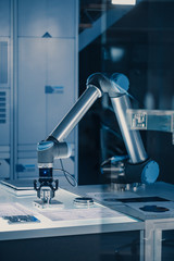 Leinwandbilder - Vertical Shot of Futuristic Artificial Intelligence Robotic Arm Operates and Moves a Metal Object, Picks It Up and Puts it Down. Scene is Taken in a High Tech Research Laboratory with Modern Equipment