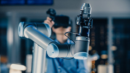 Leinwandbilder - Close-up Shot of a Futuristic Robotic Arm Controlled by Professional Development Engineer with Virtual Reality Headset and Joysticks in a High Tech Research Laboratory with Modern Equipment