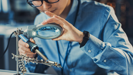 Leinwandbilder - Close Up of a Professional Japanese Development Engineer in Blue Shirt Soldering a Circuit Board in a High Tech Research Laboratory with Modern Computer Equipment.