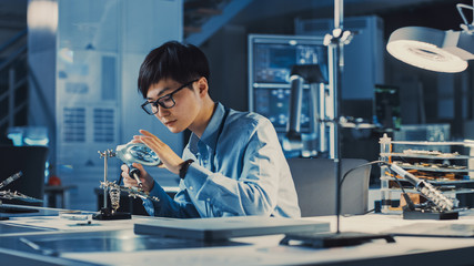 Leinwandbilder - Professional Japanese Electronics Development Engineer in Blue Shirt is Soldering a Circuit Board in a High Tech Research Laboratory with Modern Computer Equipment.