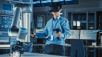 Leinwandbilder - Professional Japanese Development Engineer in Blue Shirt is Controlling a Futuristic Robotic Arm with a Virtual Reality Headset and Joysticks in a High Tech Research Laboratory with Modern Equipment.