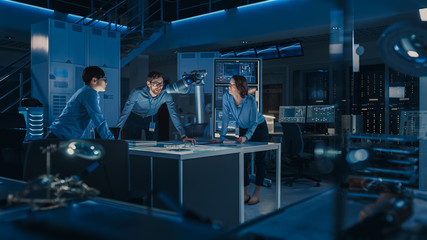 Leinwandbilder - Futuristic Metal Robotic Arm is Moving a Metal Object. Senior Engineer Talks Through This Advanced Process with His Diverse Team. They are in a High Tech Research Laboratory with Modern Equipment.