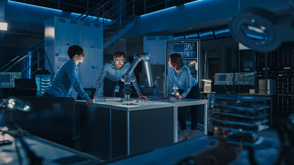 Leinwandbilder - Futuristic Robotic Arm is Moving and Placing a Metal Object. Senior Engineer Talks Through This Advanced Process with His Diverse Team. They are in High Tech Research Laboratory with Modern Equipment