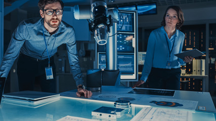 Poster - Futuristic Robotic Arm Moving and Placing a Metal Object. Senior Engineer Talks Through This Advanced Process. They are in a High Tech Research Laboratory with Modern Equipment.
