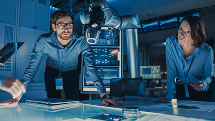 Leinwandbilder - Diverse Team of Engineers with Laptop and a Tablet Analyse and Discuss How a Futuristic Robotic Arm Works and Moves a Metal Object. They are in a High Tech Research Laboratory with Modern Equipment.