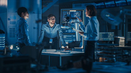 Leinwandbilder - Diverse Team of Engineers with Laptop and a Tablet Analyse and Discuss How a Futuristic Robotic Arm Works and Moves a Metal Object. They are in a High Tech Research Laboratory with Modern Equipment.
