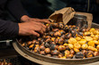 Close up of hands of chestnut vendor roasting chestnuts on a street, preparing a serving in a paper bag