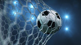 Fototapeta Pokój dzieciecy - Soccer ball flew into the goal. Soccer ball bends the net, against the background of flashes of light. Soccer ball in goal net on blue background. A moment of delight. 3D illustration