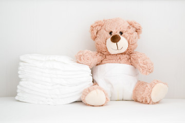 brown teddy bear sitting in baby bed. stack of white diapers. front view. closeup.