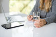 © Dominika - A blonde hair businesswoman working in her workstation. Businesswoman working at the desk at workplace. Woman working in home office. Woman sitting at desk and working with laptop and glass of water.