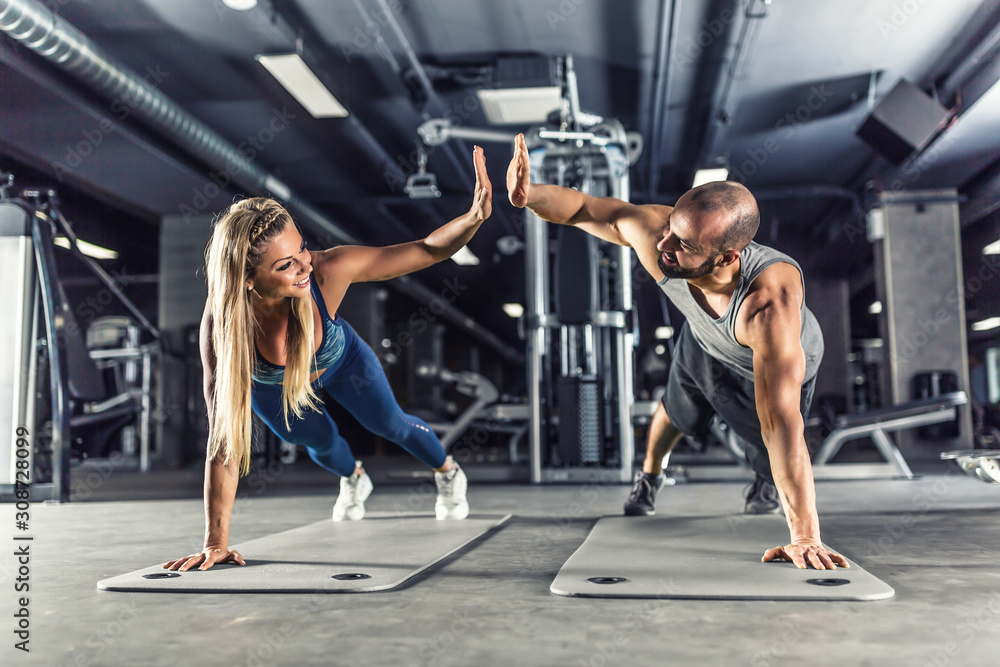 Sport couple doing plank exercise workout in fitness centrum. Man and woman practicing plank in the gym - obrazy, fototapety, plakaty 