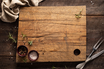 chopping board on dark, wooden table. rosemary, pepper, salt. copy space.