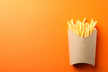 Wall Mural - Slices of hot french fries in box on orange background, space for text. Top view