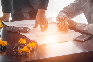 Management consulting with engineers or architects working at construction site and holding blueprint in his hand for management business plan.