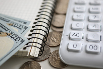 Blank notebook page and white calculator lying at pile of US dollars