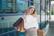 Young attractive pregnant blonde woman in a white sweater against the backdrop of the city streets. Holding a lot of shopping bags.