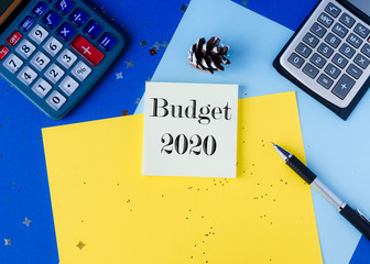 budget 2020 concept. Flat lay with colorful paper, pen and calculator on blue background