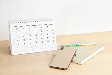 Poster - Paper calendar and smartphone on wooden table near white wall