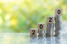 2020 New Year, Money And Business Concept. Close Up Of Number Wooden Block Toy On Top Unstable Stack Of Coins With Bokeh Green Leaf Nature Background And Copy Space.