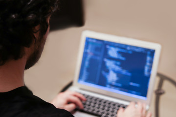 young man is developing complex software on laptop on blurred background. view from the back without